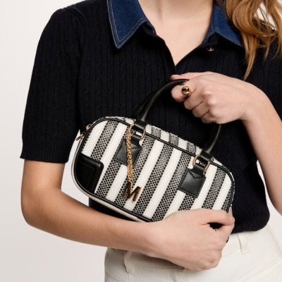 Mala pequena às riscas pretas e brancas com detalhes dourados, segurada por mulher com camisa preta e calças brancas