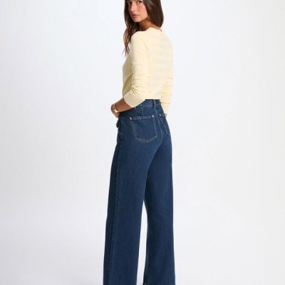 Mulher de costas com calças de ganga azuis e camisola creme em fundo branco