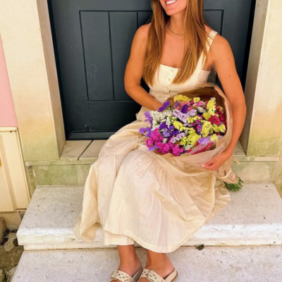 Mulher com vestido bege e sapatos rasos, sentada com um bouquet colorido