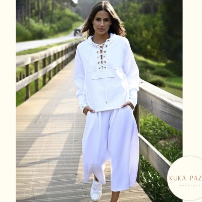 Mulher em passadeira de madeira ao ar livre com casaco branco e calças largas brancas