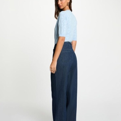 Mulher a usar camiseta azul clara e calças largas de ganga azul escuro em fundo branco