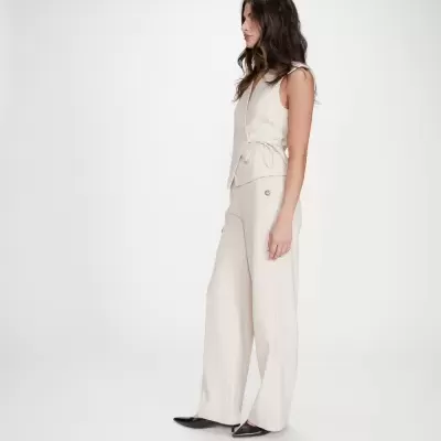 Mulher com colete bege e calças largas bege com sapatos pretos.