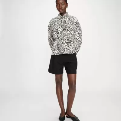 Mulher com camisa padrão zebra, calções pretos e sapatos pretos em fundo branco.