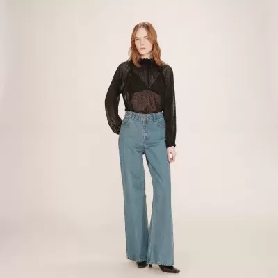 Mulher vestindo calças largas de ganga azuis com blusa preta transparente de bolinhas e sapatos pretos.