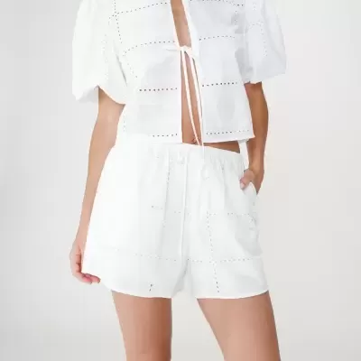 Conjunto de verão branco feminino com camisa curta e calções, padrão perfurado, em fundo neutro