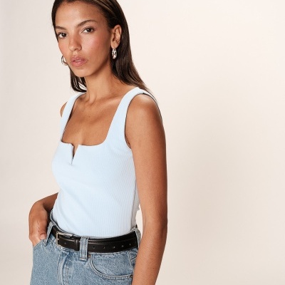 Mulher com regata azul clara e calças de ganga azuis com cinto preto