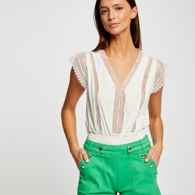 Mulher com blusa branca de renda e calções verdes com botões