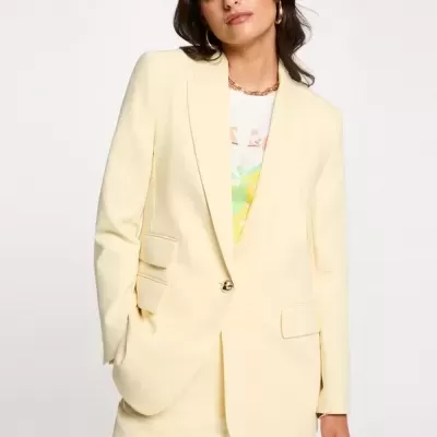 Conjunto feminino amarelo claro com blazer e calças, usado com t-shirt branca e acessórios dourados