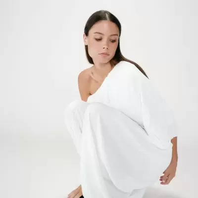 Mulher vestindo vestido branco texturado ombro a ombro, sentada em fundo branco