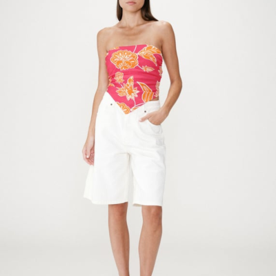 Mulher com top bandeau vermelho estampado e calções brancos.