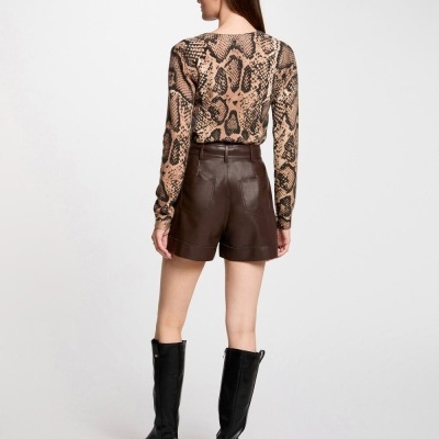 Mulher de costas com blusa padrão pele de cobra, calções de pele castanhos e botas pretas