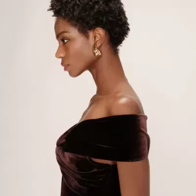 Mulher com vestido de veludo castanho escuro e brinco dourado