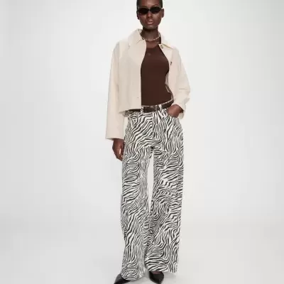 Mulher com casaco bege, camisola castanha, calças com padrão zebra e óculos de sol