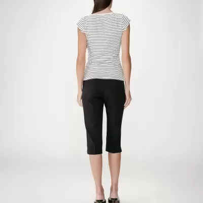 Mulher de costas com t-shirt de riscas pretas e brancas, calças capri pretas e sapatos de salto pretos.