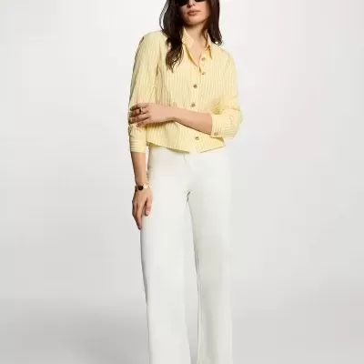 Mulher com camisa amarela às riscas, calças brancas largas e sapatos dourados rasos