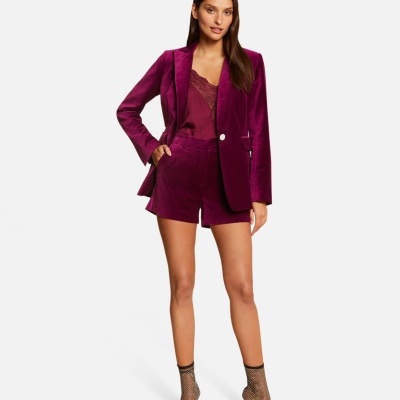 Mulher a usar conjunto de blazer e calções em veludo vinho com top rendado e sandálias de salto alto