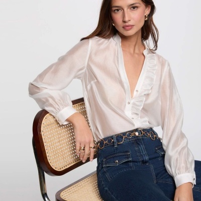 Mulher a usar blusa branca de folhos e calças de ganga azul sentado numa cadeira com assento e encosto em palhinha.