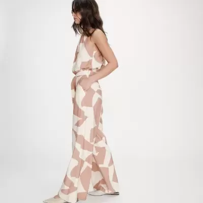 Mulher a usar macacão comprido bege com padrão castanho claro e sapatos baixos creme