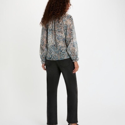 Mulher de costas com camisa estampada e calças pretas num fundo branco