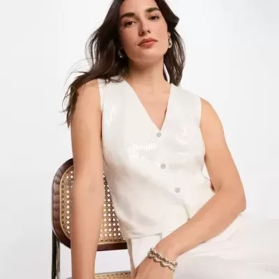 Colete branco feminino sentado numa cadeira de metal com assento em vime