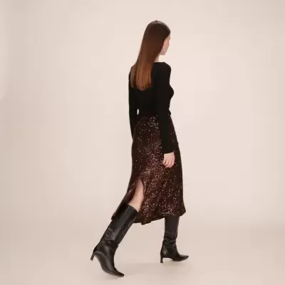 Mulher de costas com saia castanha com lantejoulas, camisola preta e botins pretos