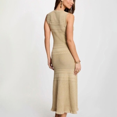Mulher de costas vestindo vestido comprido bege com texturas detalhadas e sandálias com tachas