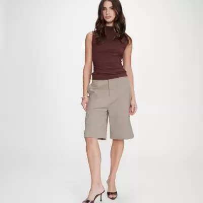 Mulher com blusa castanha sem mangas e calças bermuda bege claras