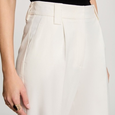 Calças brancas com bolso lateral e pregas frontais usadas com camisola preta
