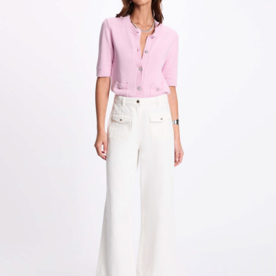 Mulher vestindo cardigan rosa e calças brancas em fundo branco.