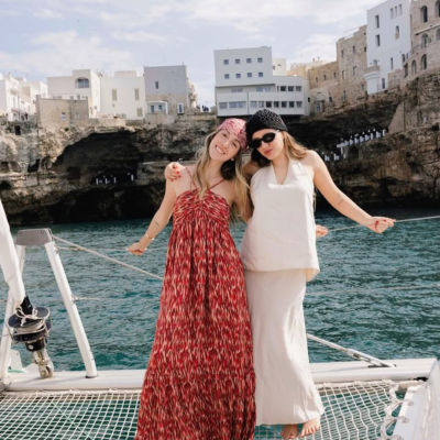 Duas mulheres em vestidos elegantes na rede de um catamaran com mar e edifícios ao fundo