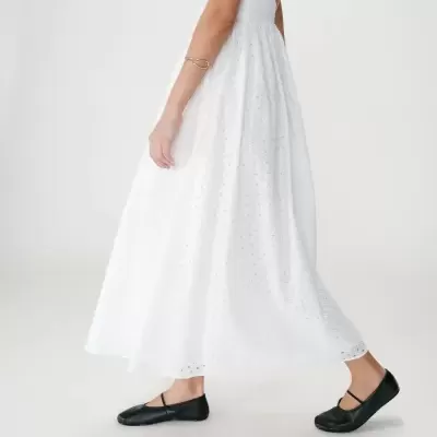 Vestido branco comprido com bordado inglês e sapatos baixos pretos.
