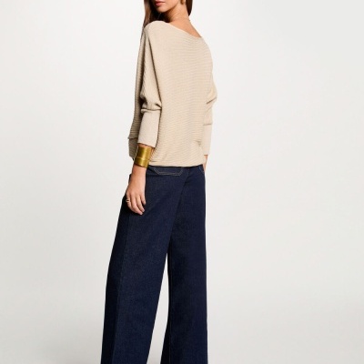 Mulher vestida com camisa de malha bege, calças largas azul escuro e botins pretos de salto