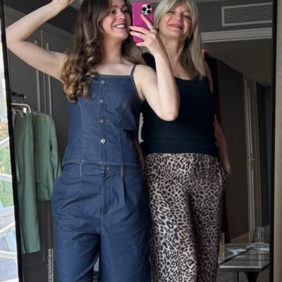 Duas mulheres tirando selfie no espelho com roupa casual, incluindo jardineira de ganga e calças de estampa animal.