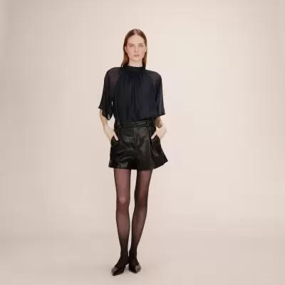 Mulher com blusa preta, calções de pele pretos e meia-calça preta