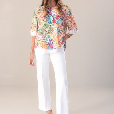 Mulher com blusa floral colorida, calças brancas e sandálias douradas de salto alto