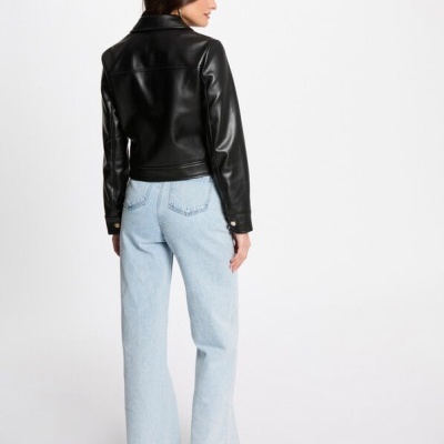 Mulher de costas a usar casaco preto tipo pele, calças de ganga azul claro e sapatos pretos em fundo branco