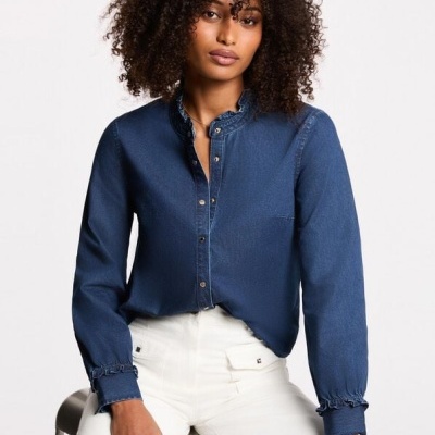 Mulher com camisa denim azul escura e calças brancas num fundo claro