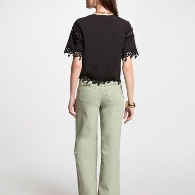 Mulher de costas com t-shirt preta com renda, calças verdes largas e sapatos pretos