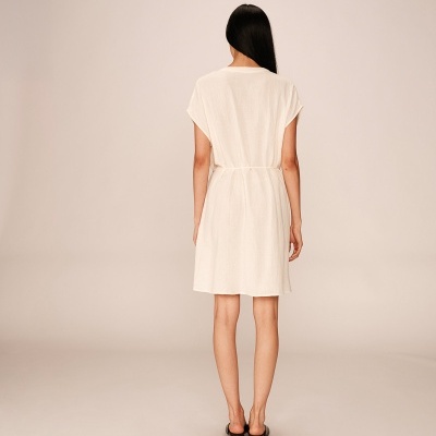 Mulher de costas a usar vestido curto branco com textura e cordão na cintura.