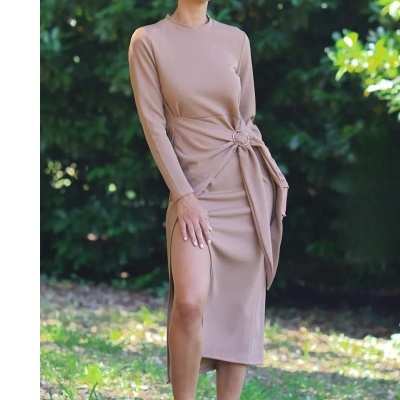 Vestido comprido castanho claro com nó decorativo e racha lateral usado por mulher ao ar livre