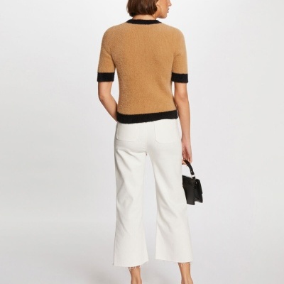 Mulher de costas com camisola castanho claro e calças brancas em fundo branco