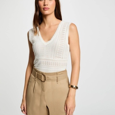 Mulher a usar top branco rendado e calções bege com cinto em fundo branco.