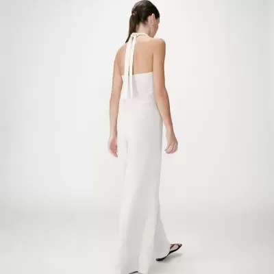 Vestido longo branco sem mangas, alças amarradas no pescoço, tecido leve, usado com chinelos pretos