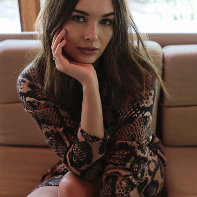 Mulher com vestido animal print castanho e preto sentada num sofá bege.