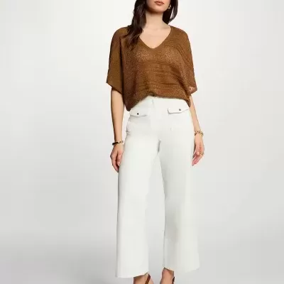 Mulher de blusa castanha, calças brancas e sapatos castanhos de salto em fundo branco