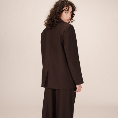 Mulher vista de costas a usar blazer preto e calças largas no fundo neutro