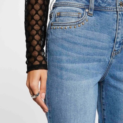 Calças de ganga azul claro com tachas metálicas e blusa preta transparente