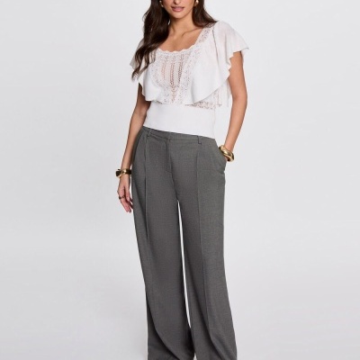 Mulher vestindo blusa branca com renda e folhos e calças largas cinza