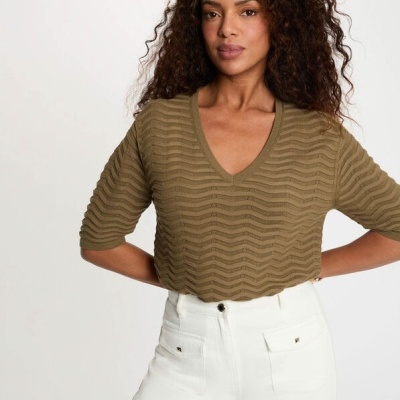 Mulher com top verde texturizado e calças brancas com bolsos frontais