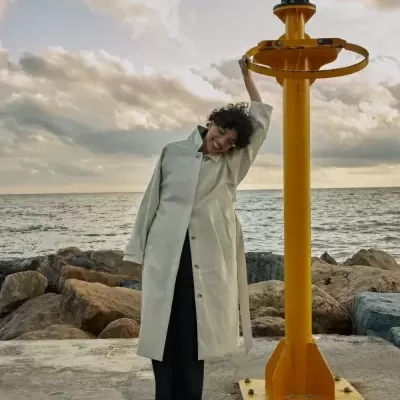 Mulher com casaco creme junto ao mar e estrutura amarela